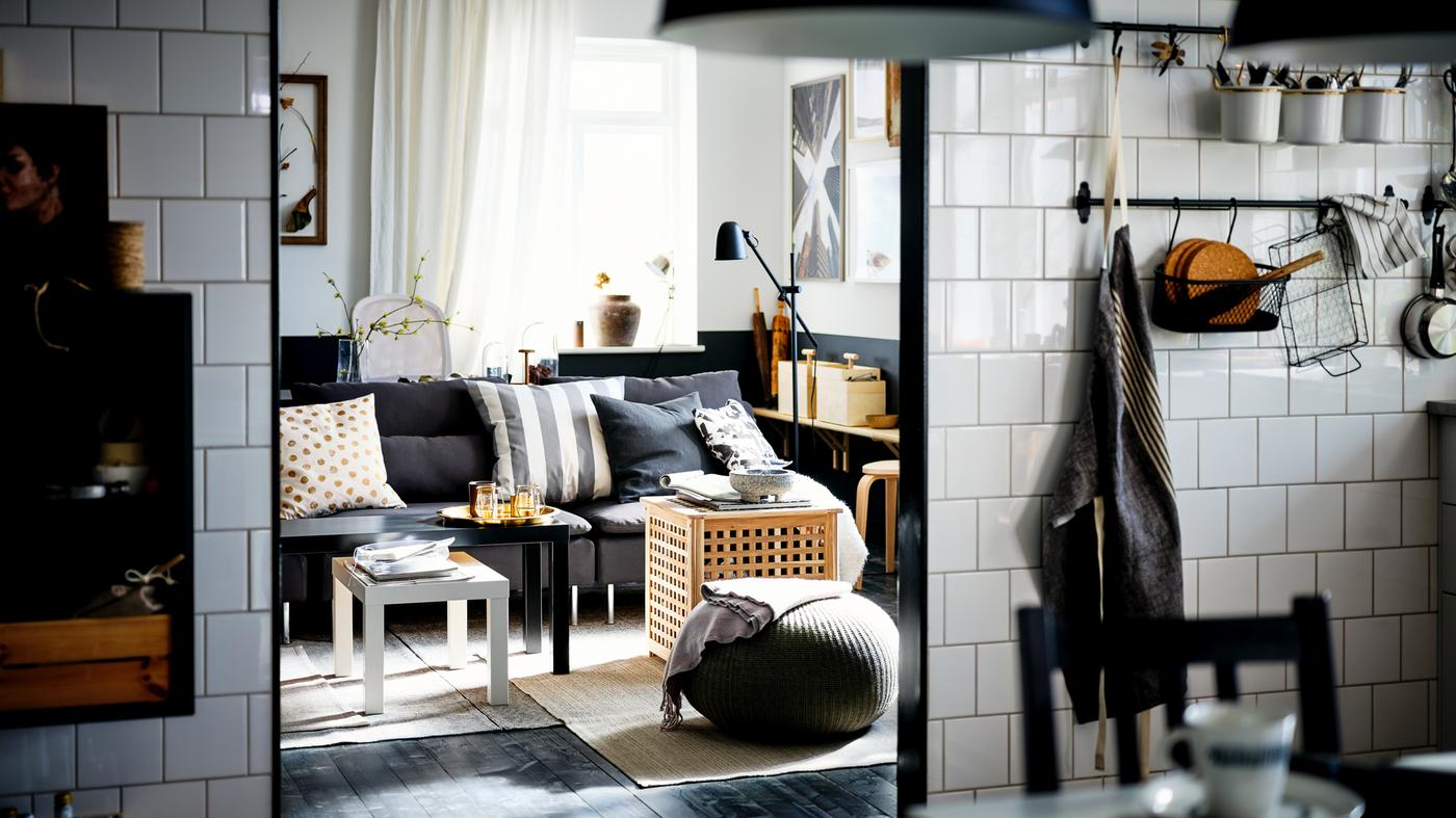 A white-tiled kitchen opening onto a living room with a dark-gray SÖDERHAMN sofa and black and white LACK nesting tables.