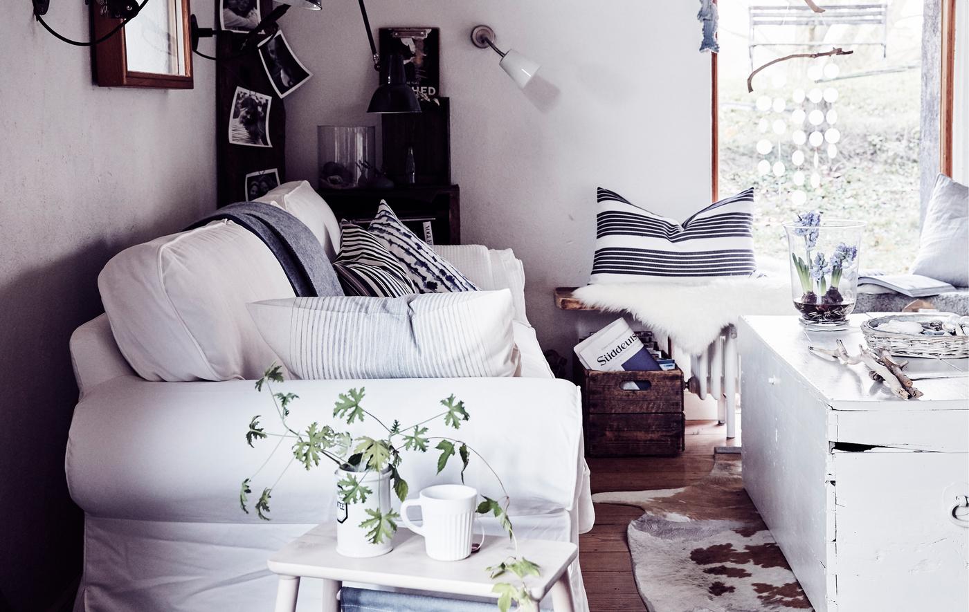 A white traditional-style sofa in a living room with striped cushions, vintage wooden trunk and natural materials.