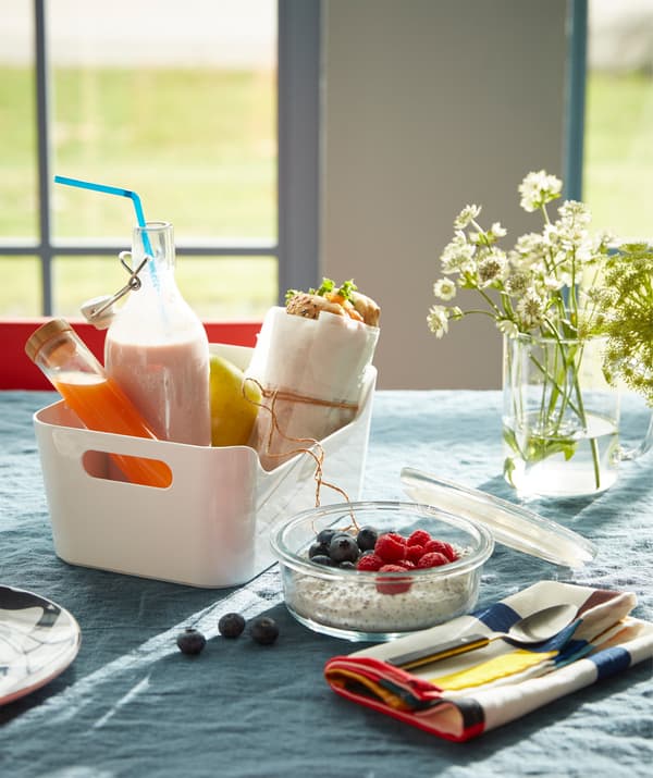A white VARIERA box filled with a sandwich, a yoghurt glass bottle and juice for a takeaway breakfast.