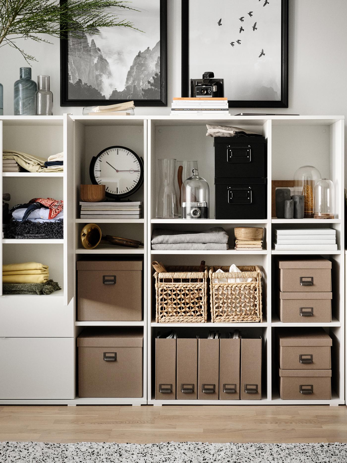 A white VIHALS storage unit with neatly arranged boxes and baskets, a clock, magazines, and two framed artworks above it.