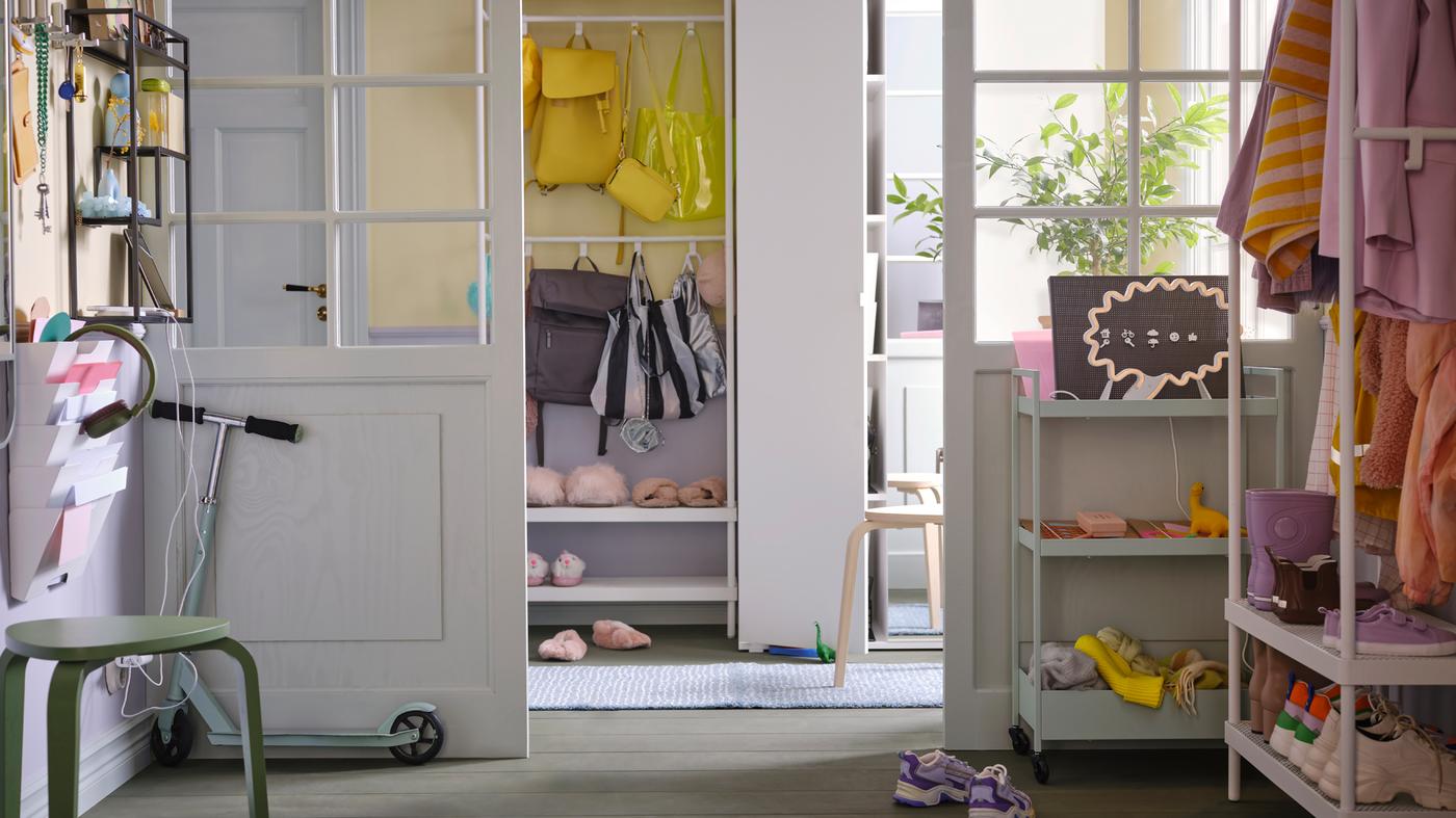 A white VIHALS wardrobe by a white MACKAPÄR coat rack with shoe storage holding colourful shoes and bags in a sunny hallway.