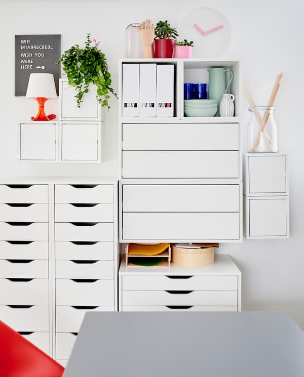 A white wall-mounted cabinet combination and white drawer units with dinnerware, decorative items and magazine files.