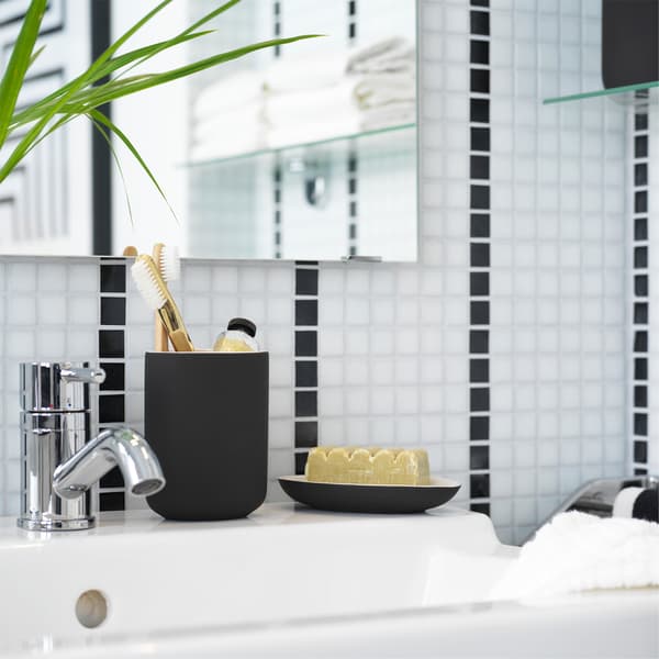 A white wash basin where toothbrushes stand in a dark grey toothbrush holder in a black/white bathroom.