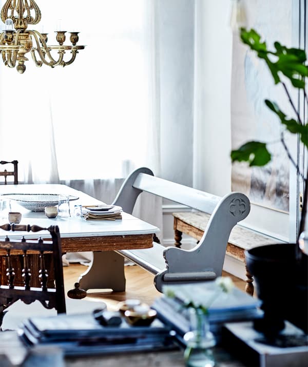 A white wooden bench alongside a table with gold chandelier above.