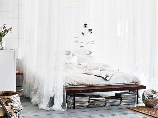 A wideshot showing a big white bed with crisp sheets and pillows and sheer white draping textiles.