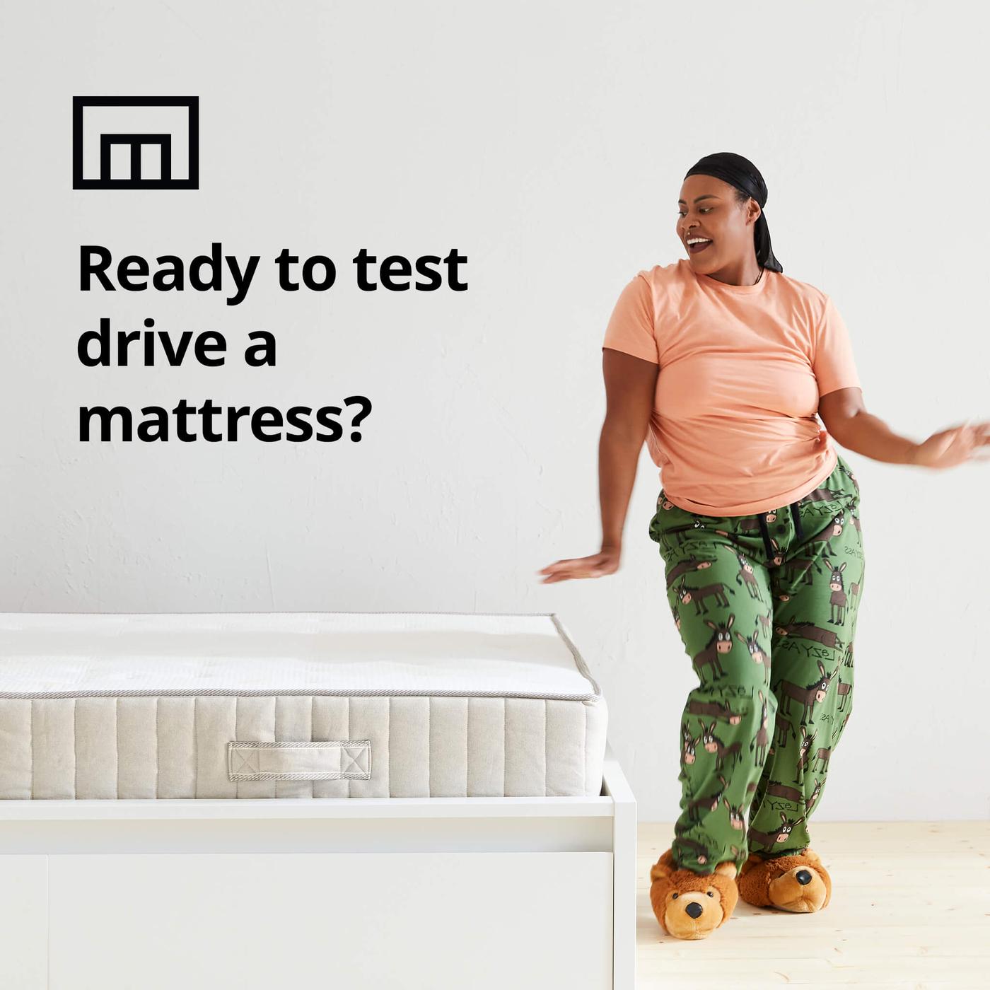 A woman dancing in her pajamas next to a bed and a store box symbol and the text 'Ready to test drive a mattress?' on the image.