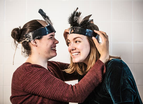 A woman helping another woman put on a harvest-themed head band.