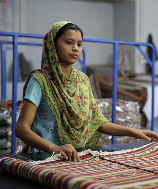 A woman holding a patterned, colourful rug on a worktop.