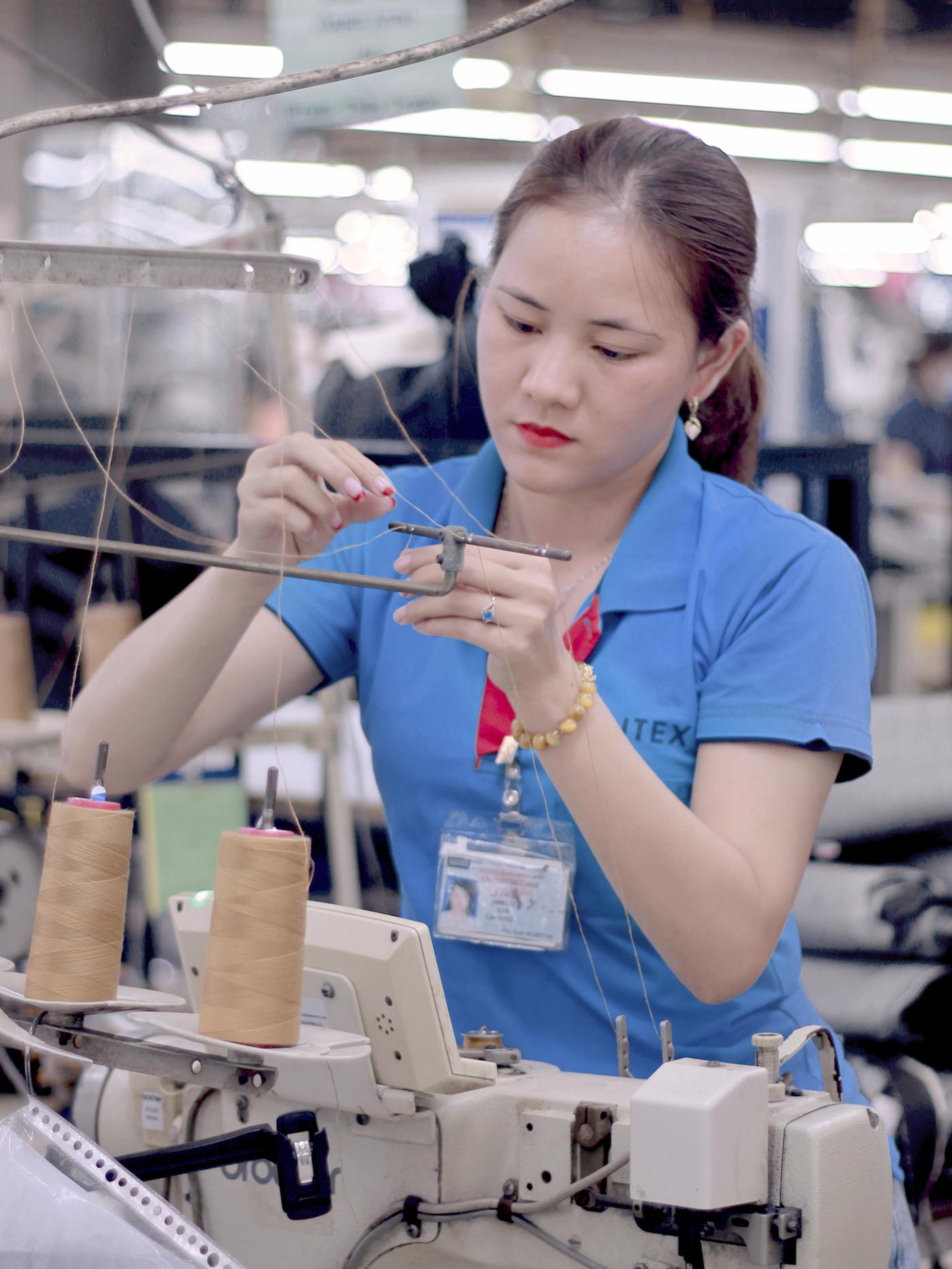 A woman in a blue shirt threads a sewing machine at a Saitex factory in Vietnam.