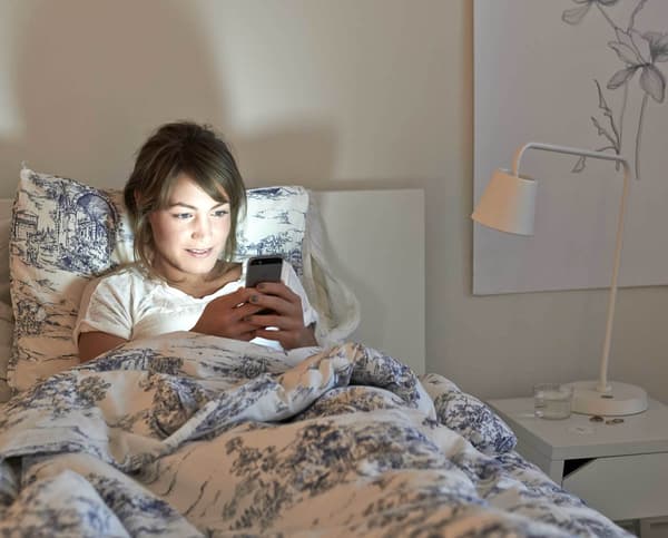 A woman in bed looking at a mobile device.