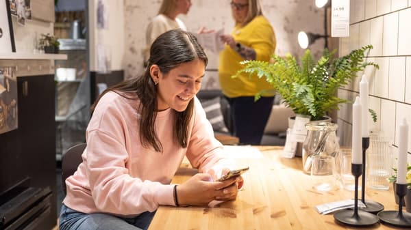 A woman is sitting at a table with a table lamp, looking something up on her phone.