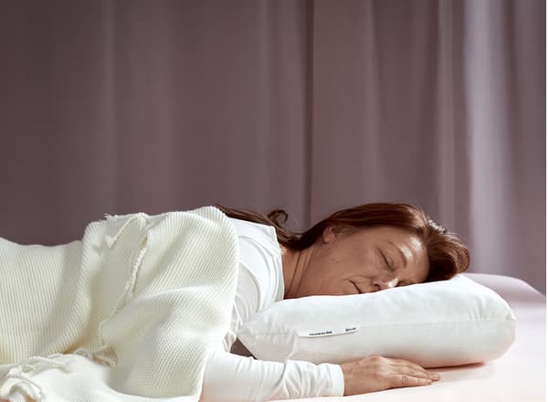 A woman, laying on her stomach, is sleeping deeply on IKEA SKOGSLÖK ergonomic pillow.