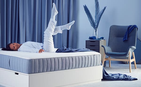 A woman lying on a mattress with her legs in the air in comfort, with blue curtains behind her.