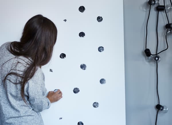 A woman making black dot pattern on a white plywood sheet.