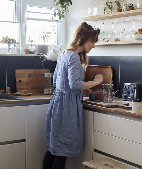 A woman making tea in the corner of a blue and white kitchen.