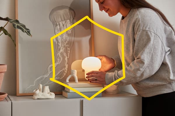 A woman places a small table lamp on top of a stack of books.