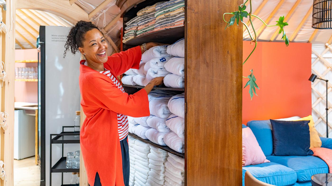 A woman puts towels into a high wooden cabinet in a yurt
