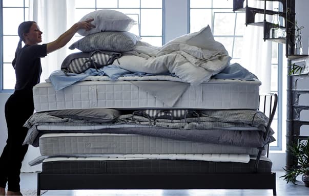 A woman putting a pillow on top of a stack of soft mattresses, quilts and bed textiles