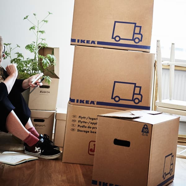 A woman sitting on a wooden floor surrounded by various boxes including a pile of JÄTTENE boxes.