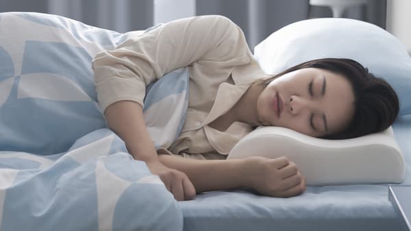 A woman sleeping on her side with her head resting on a KLUBBSPORRE ergonomic pillow.