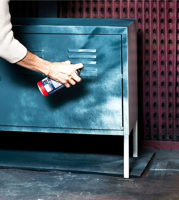 A woman spray paints a white metal cabinet blue.