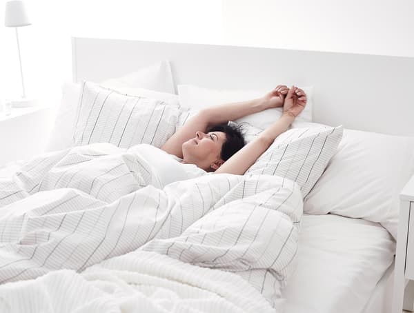 A woman stretching her arms above her head in a bed.