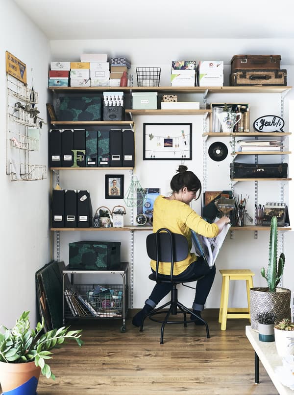 A woman using a long shelf as a desk, with shelves mounted high up on the walls to store folders, binders and boxes.