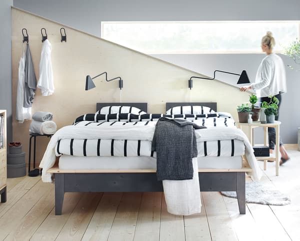 A woman walking through a bedroom with double bed and monochrome bedding.