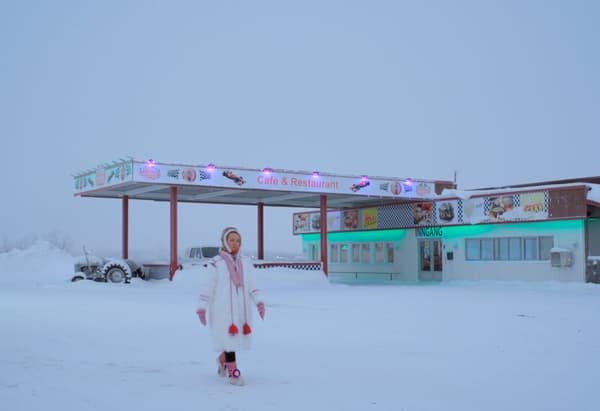 A woman walking through a deserted snowy landscape with a restaurant in the background.
