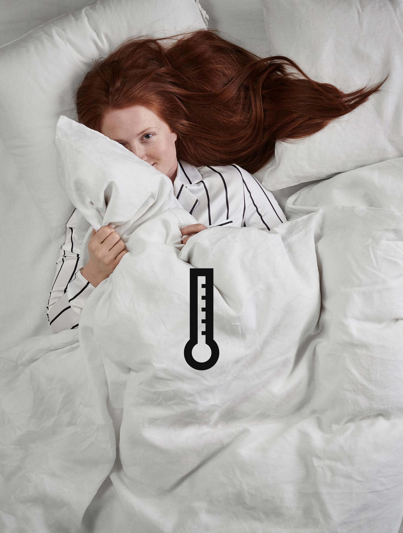 A woman with red hair lying in white bedding with a temperature icon on the image.