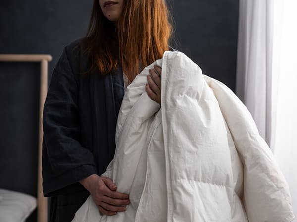 A woman with red hear holding a white duvet comforter.