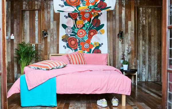 A wood-panelled bedroom with a bed dressed in pink bedding and a canopy made of colourful fabric and plants at the bedside.