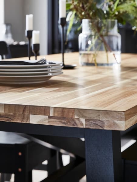 A wood-topped dining table with a striking grain pattern upon which is a pile of dinner plates, some candlesticks and a vase.