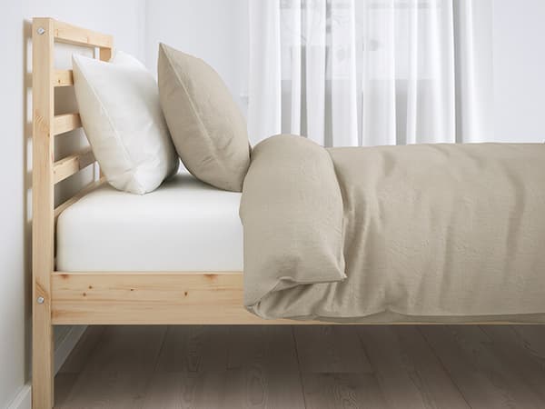 A wooden bed frame with a white mattress, pillow, and a beige pillow and comforter set.