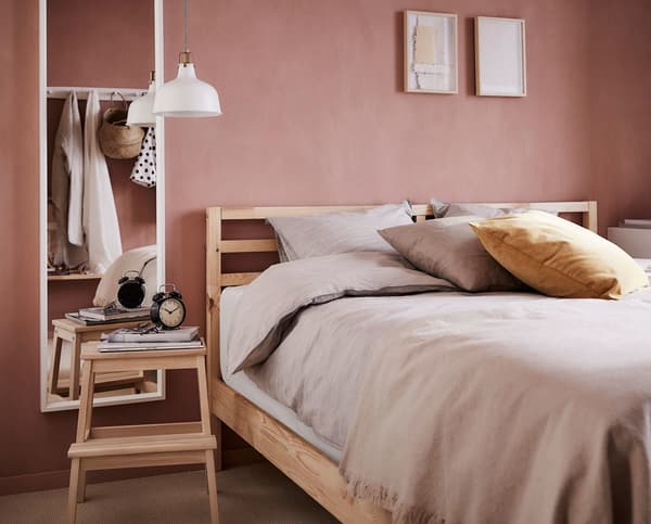 A wooden bed frame with beige bedding and a stool as a side table.