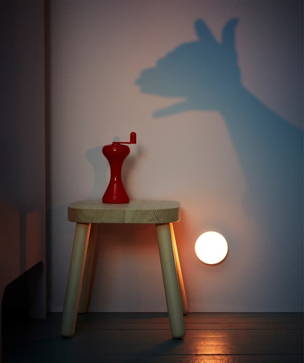 A wooden stool with a red LJUSA hand-powered flashlight and a portable light being used to cast hand puppet shadows on a wall.