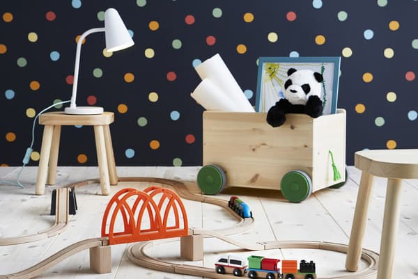 A wooden toy train set, a wooden toy crate with wheels and small wooden stools in a room with polka dot wallpaper.