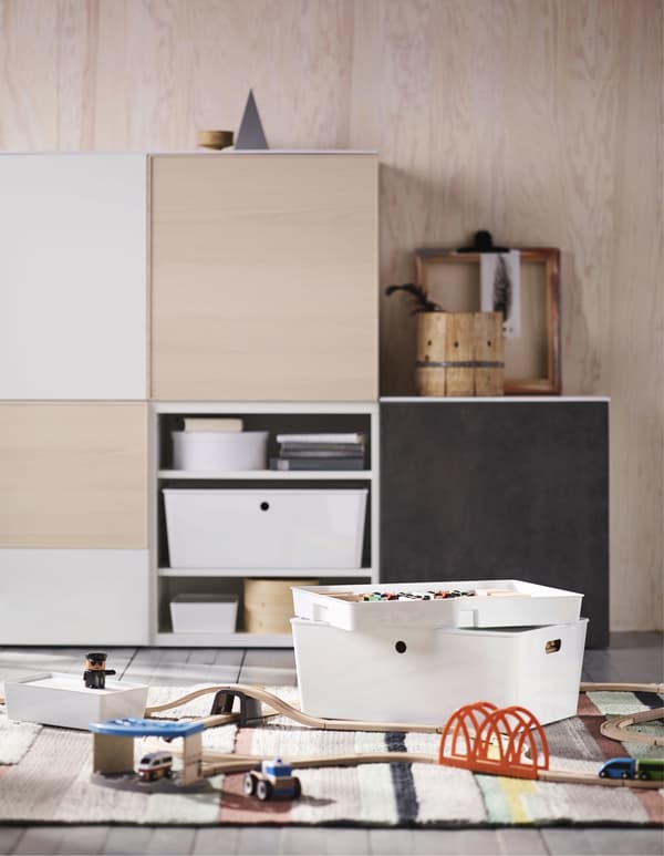 A wooden toy train set on a rug, with storage furniture and boxes in the background.