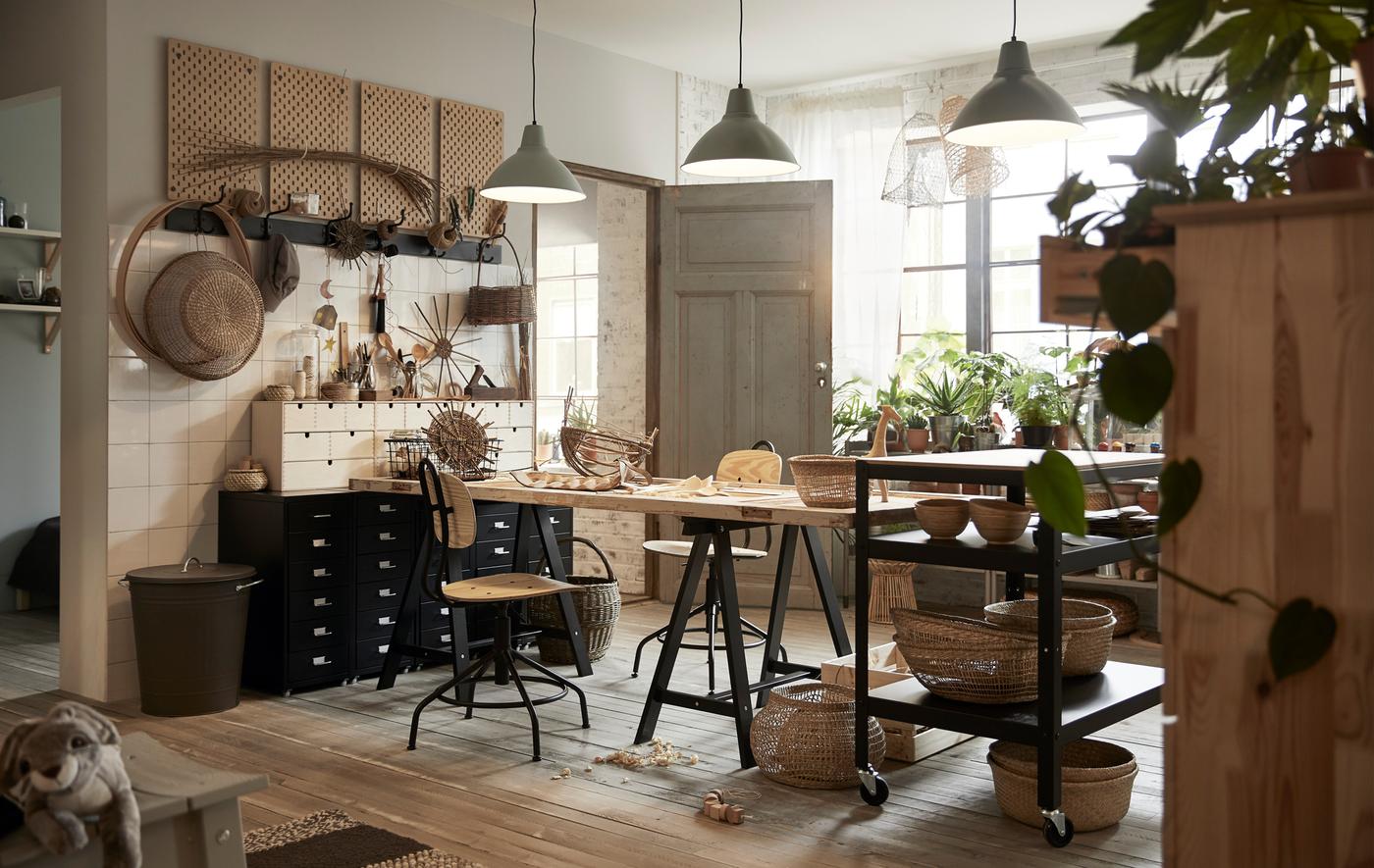 A workroom area filled with tables, swivel chairs, filing cabinets, hooks, baskets and plants.