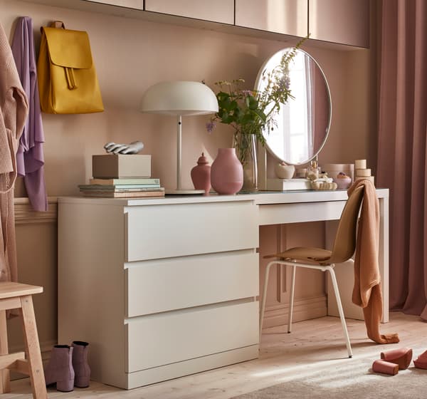 A workspace in a pink room with a white desk and dresser.