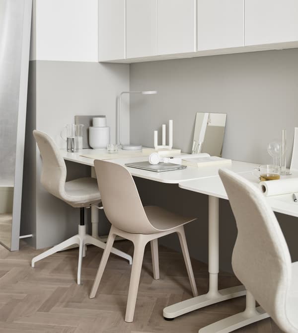 A workspace made up of two desks against the wall of a cream-coloured living room with light wood floors.