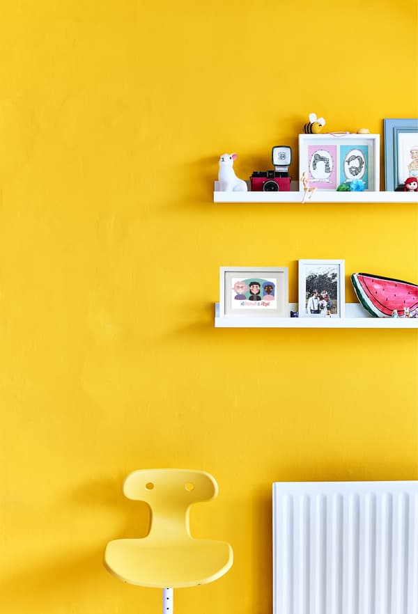 A yellow chair against a yellow wall with shelves.