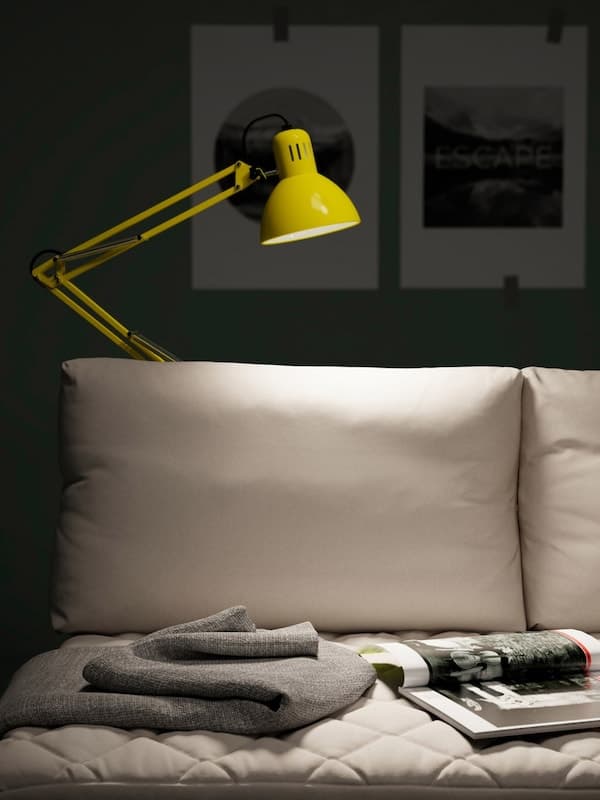 A yellow IKEA TERTIAL portable work lamp comes with an adjustable head and arm. Here it illuminates a reading zone on a sofa.