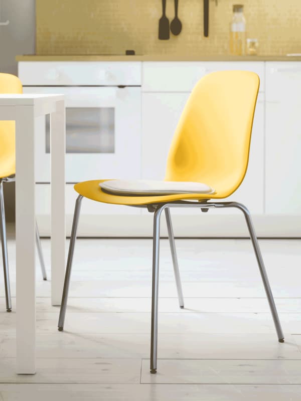 A yellow plastic dining chair with chrome legs, pulled away from a wooden dining table, in a room with wooden floorboards.