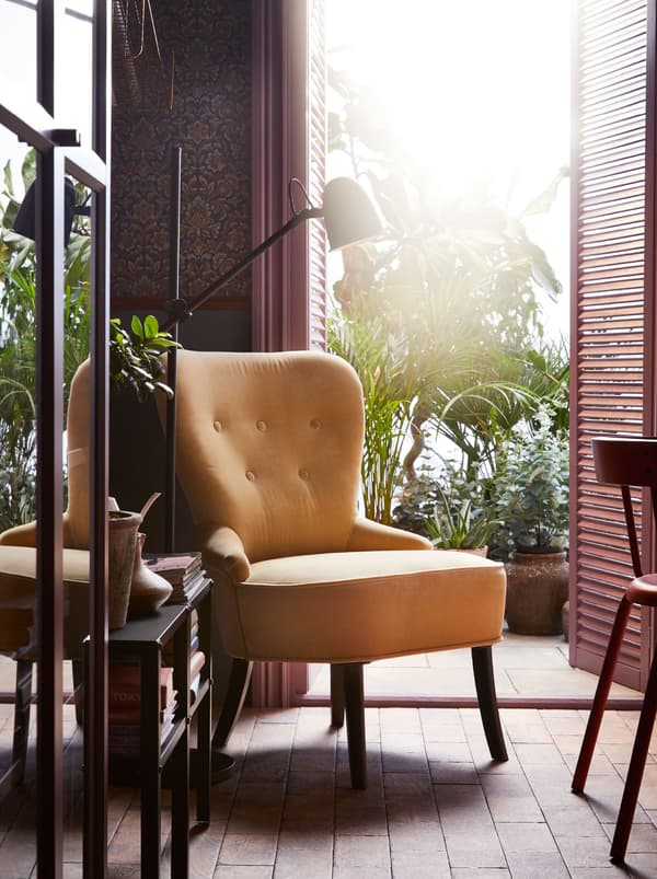 A yellow REMSTA armchair by a door opening onto a planted terrace. A black floor lamp and table with books is beside it.