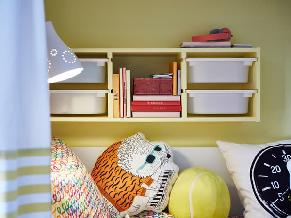 A yellow wall above a bed with a children’s TROFAST storage unit from IKEA also painted yellow.
