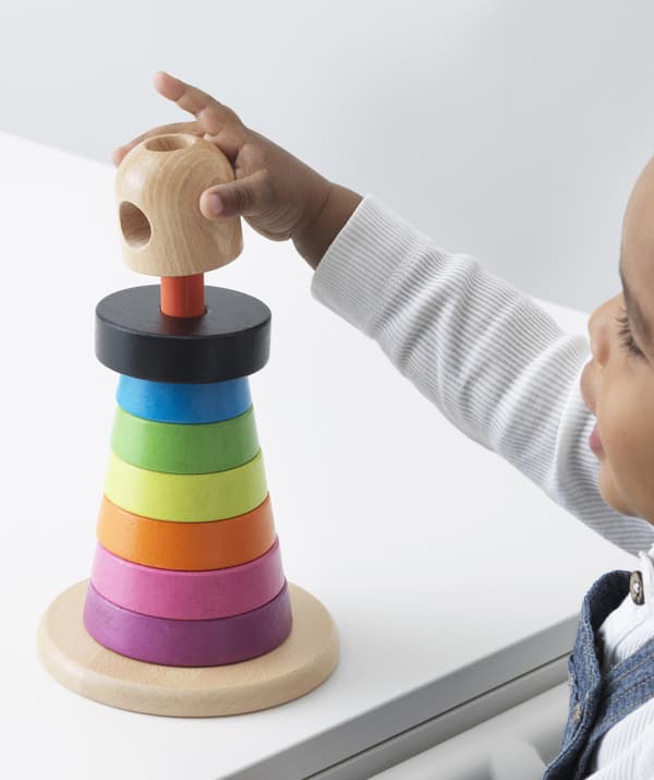 A young child plays with colourful wooden stacking rings.