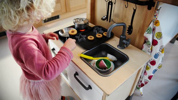 A young girl in front of a wooden play kitchen.