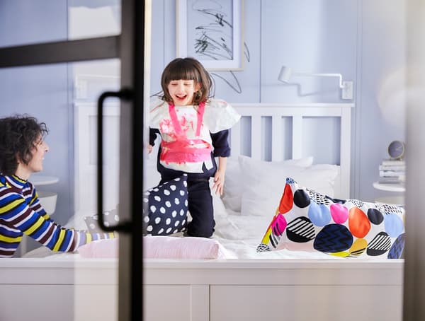 A young girl jumping on a white double bed.