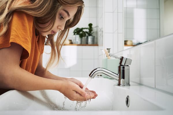A young girl wearing a t-shirt cupping water from the bathroom tap.